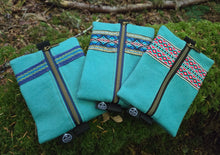 Three turquoise pouches with patterned zippers on a green mossy surface