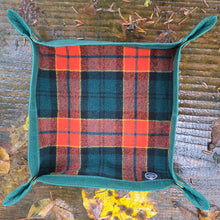 Plaid fabric square with green border on a wooden surface with leaves and shoes in the background