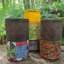 Three colorful fabric-wrapped canisters on a wooden platform with a forest background