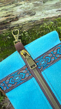 Blue bag with brown zipper and decorative strap on a natural background