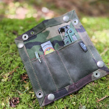 Camouflage-patterned device on a mossy surface with blurred natural background
