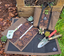 Gardening tools and accessories on a mat with a wooden stand and plants in the background