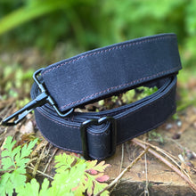 Black belt with a buckle on a natural background with leaves and grass.