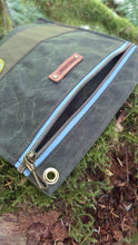Green leather clutch with gold zipper and brand logo on a natural background
