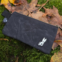 Black pouch with a logo on a green mossy surface with leaves