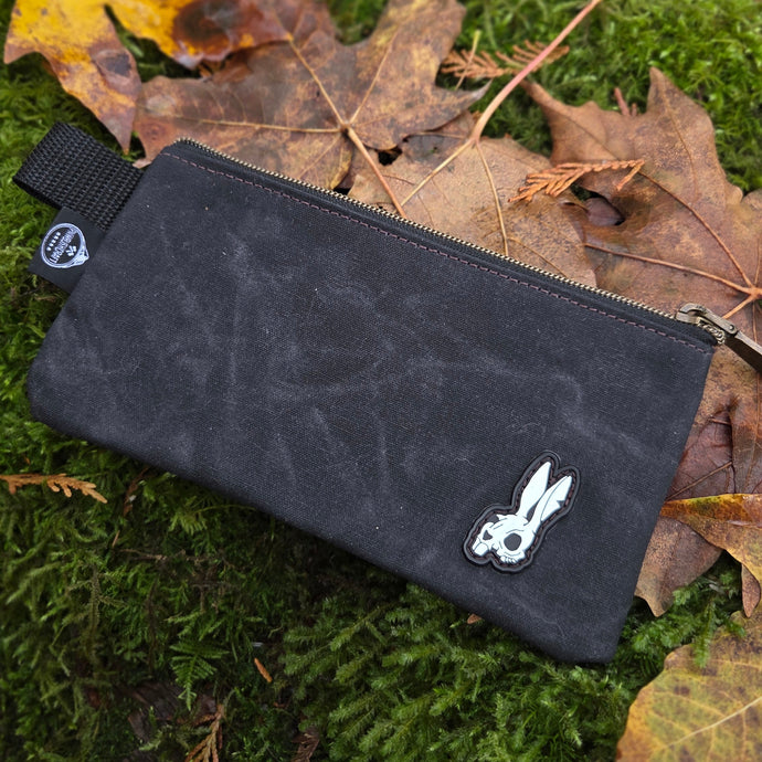 Black pouch with a logo on a green mossy surface with leaves