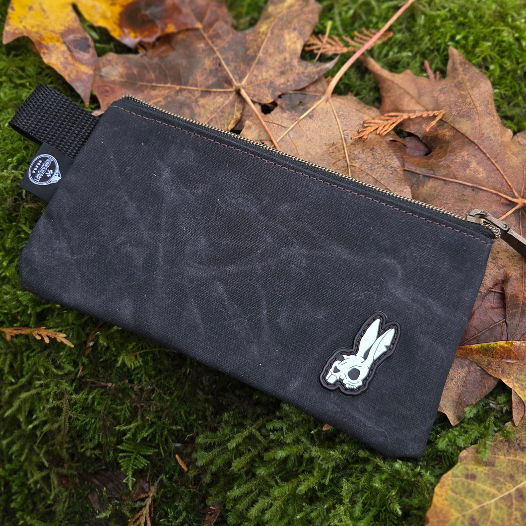 Black pouch with a logo on a green mossy surface with leaves