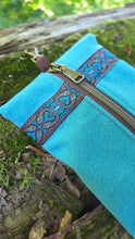 Turquoise pouch with decorative brown zipper on a natural background