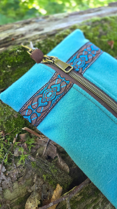 Turquoise pouch with decorative brown zipper on a natural background
