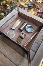 Collection of vintage items including a compass, pen, and coins in an open waxed canvas case on a wooden surface with a natural background.
