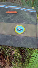 Green fabric with a patch featuring a bee design, surrounded by greenery.
