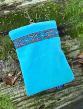 Turquoise pouch with decorative band on a wooden surface with green moss