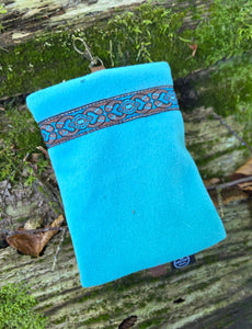 Turquoise pouch with decorative band on a wooden surface with green moss