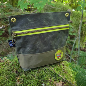 Green outdoor pouch with yellow zipper on a mossy forest background